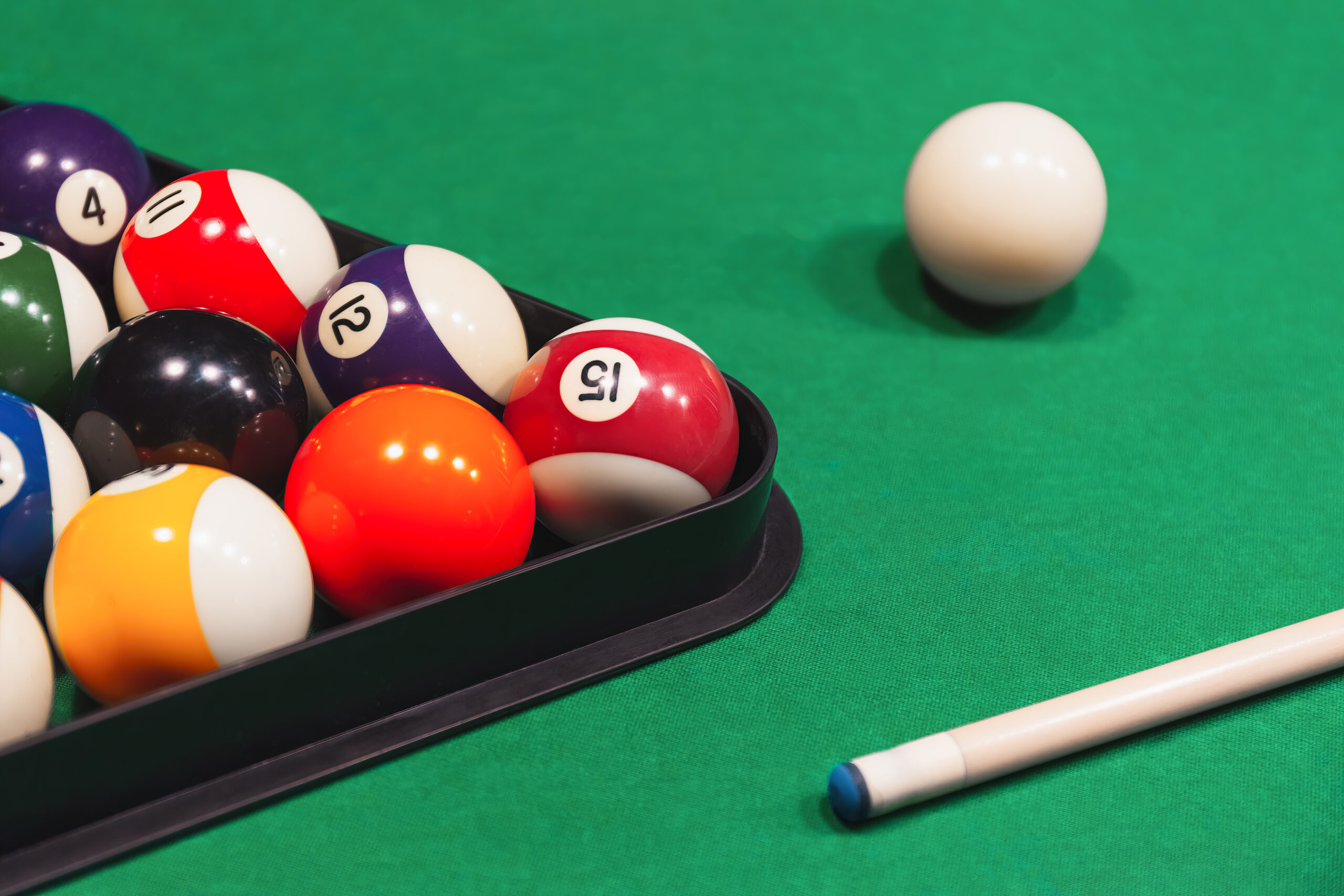 Colorful billiard balls with numbers with cue sticks and rack on green table.