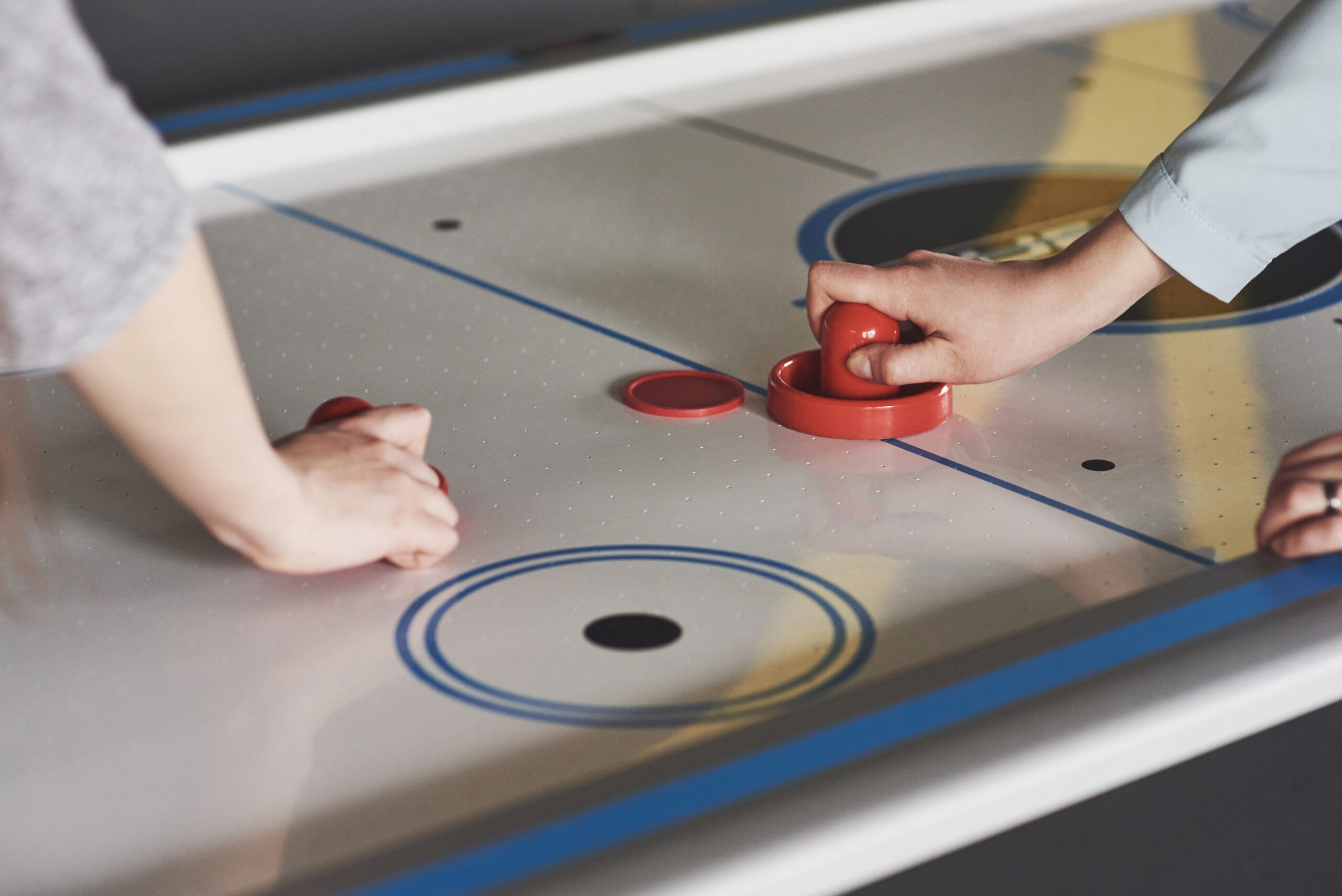 Hands of young people holding striker on air hockey table in game room.